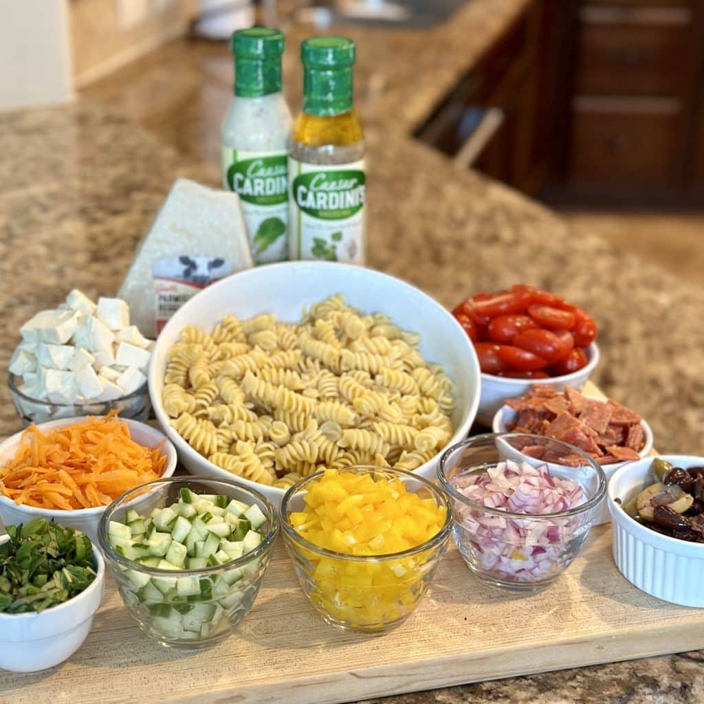 The ingredients needed to make pasta salad: veggies, dressing, cheese and noodles.