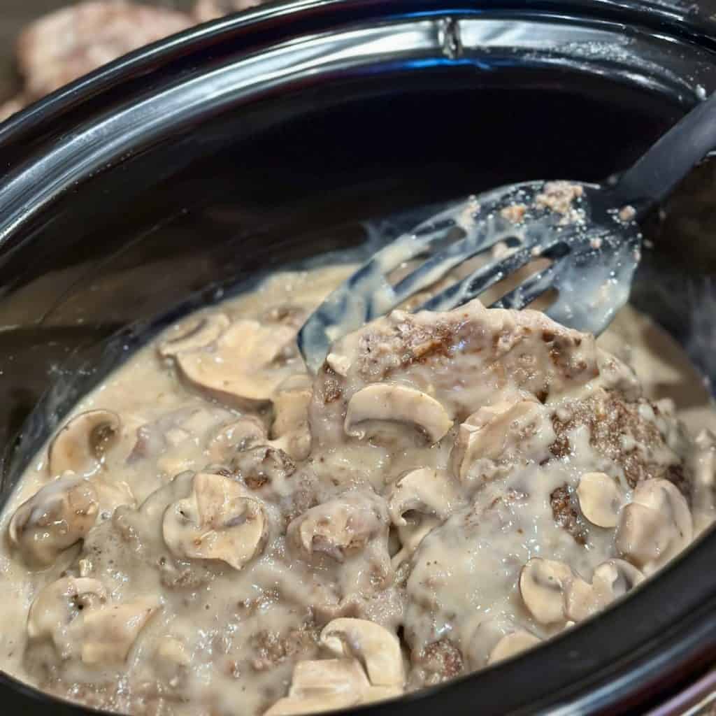 Adding cube steak to a crockpot with gravy.