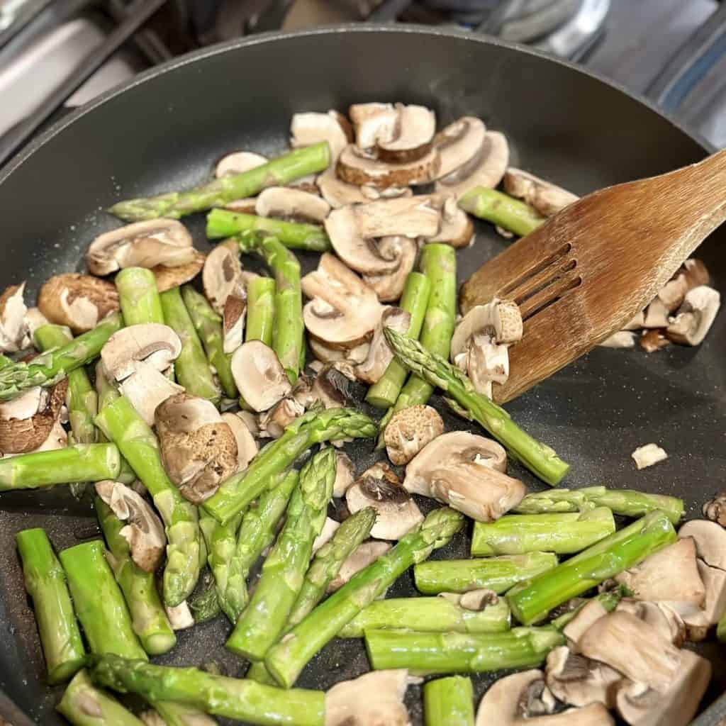 Sautéing asparagus and mushrooms in a skillet.