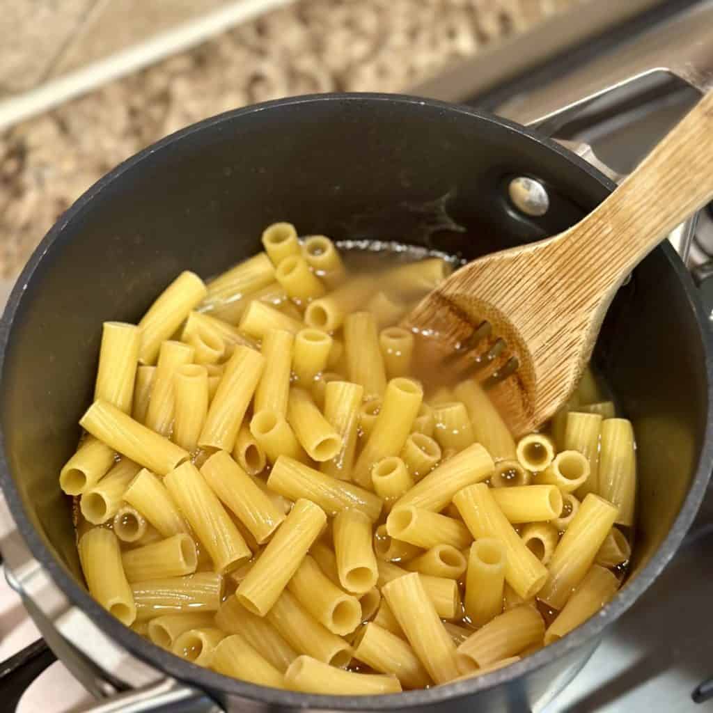 Cooking pasta in chicken broth in a pan.