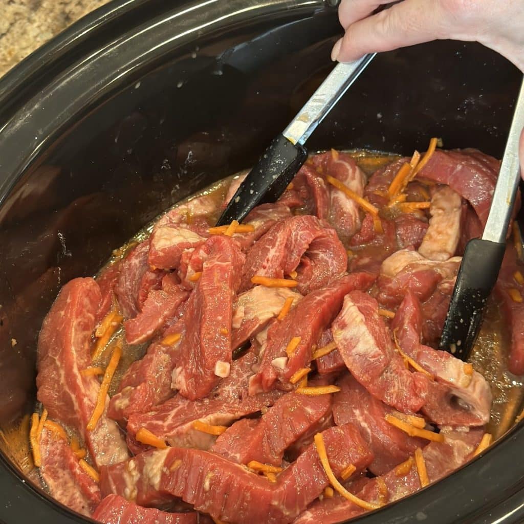 Coating flank steak in sauce in a crockpot.