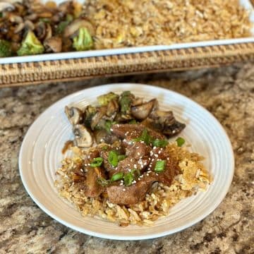 A dinner plate with fried rice, veggies and Mongolian beef.