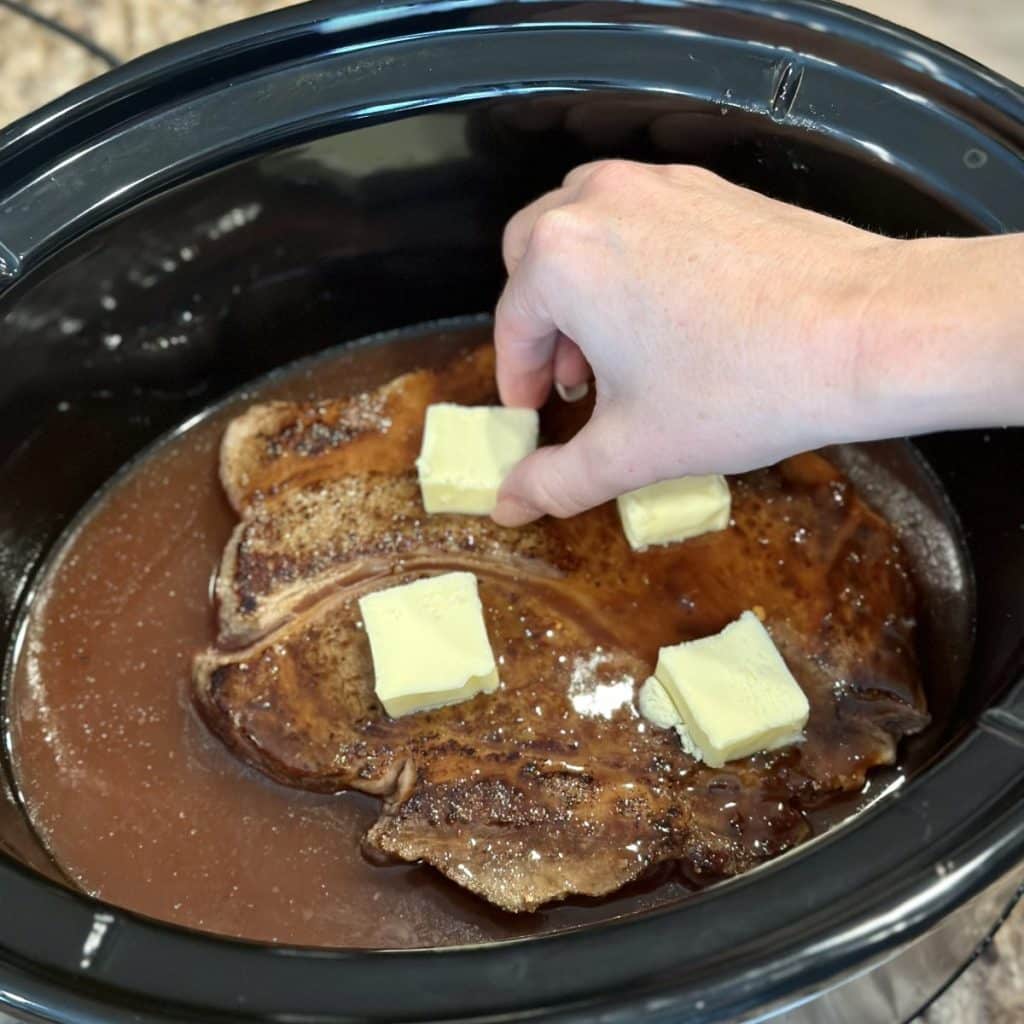 Adding butter to the top of a chuck roast in a crockpot.