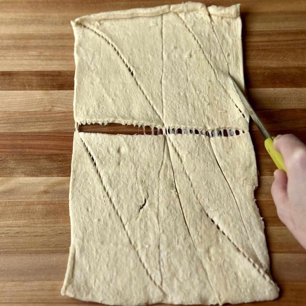 Cutting crescent roll dough in smaller triangles.