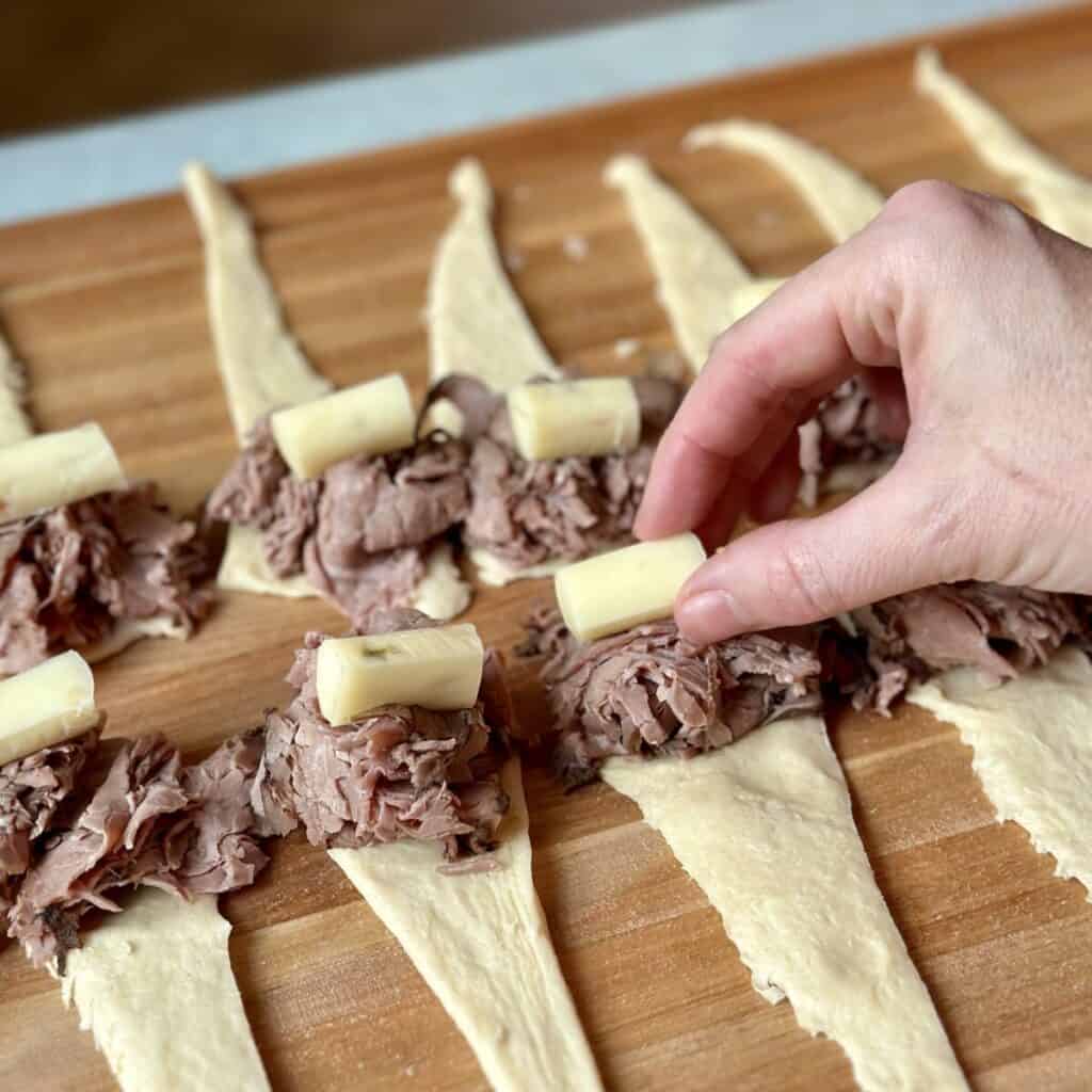 Adding cheese to the top of beef on crescent rolls.