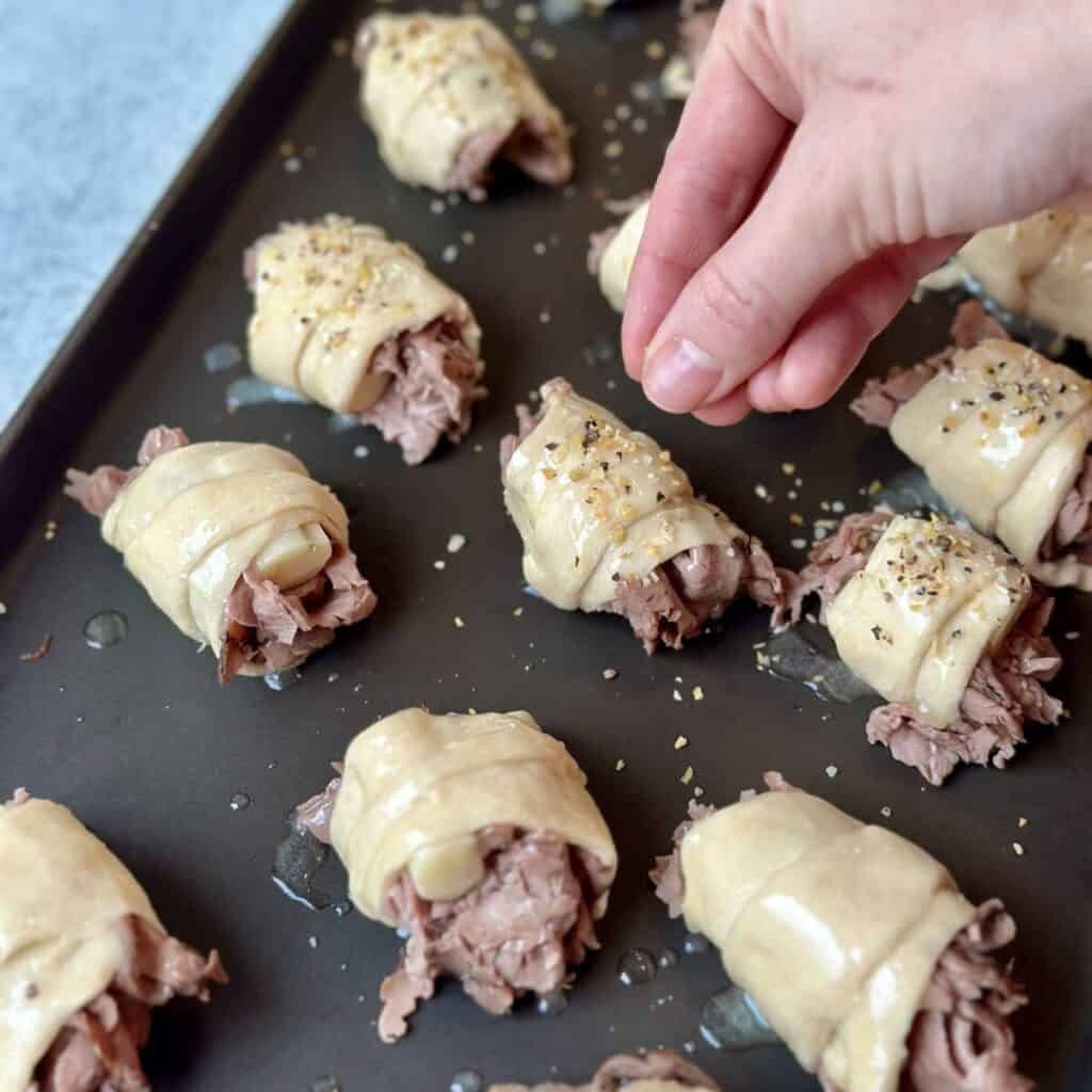 Sprinkling everything bagel seasoning on crescent roll dough.