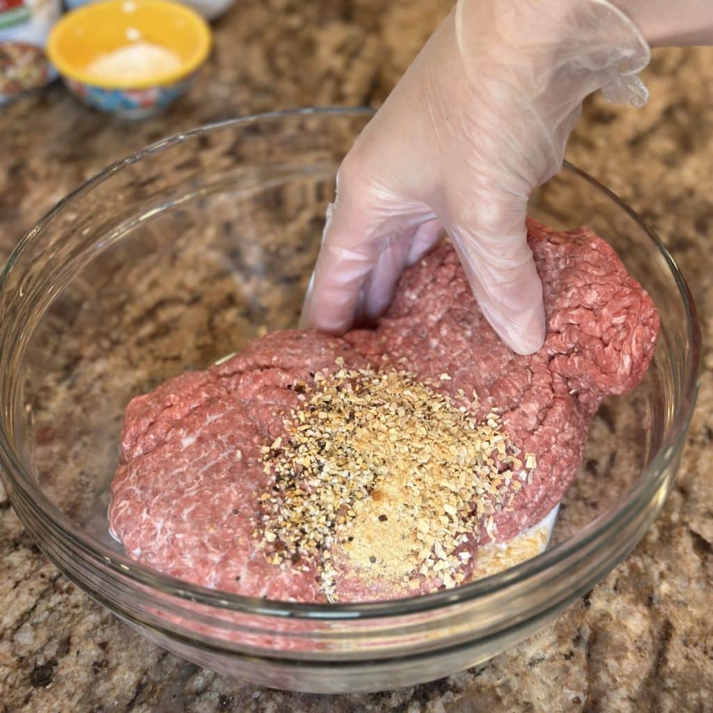 Mixing together ground beef and seasonings in a bowl.
