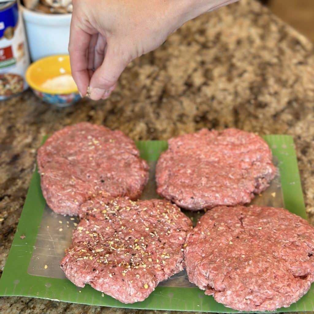 Seasoning patted out hamburger steaks.