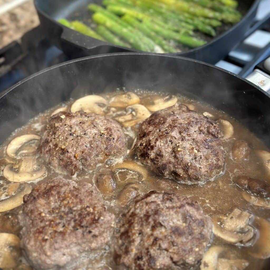 Simmering hamburger steaks in a skillet with brown gravy.