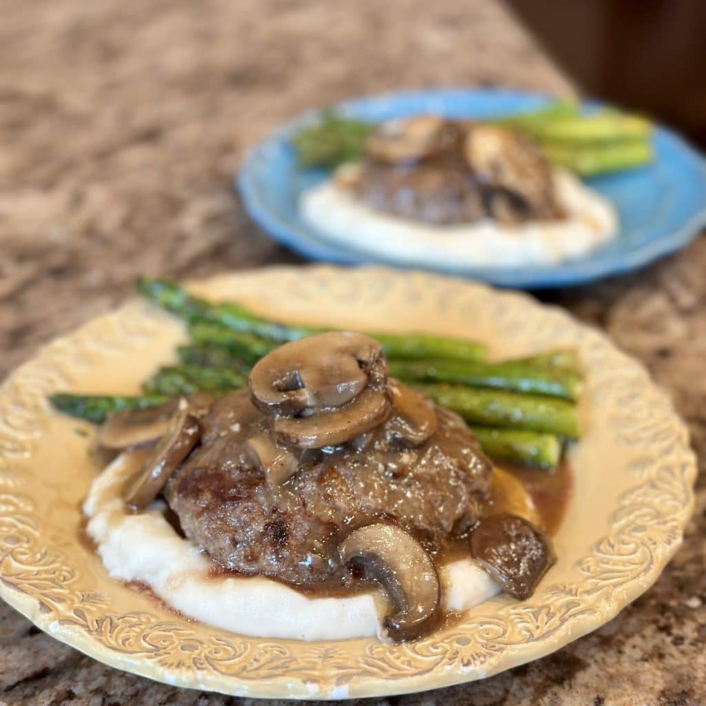 A plate with mashed potatoes, hamburger steaks, mushrooms and asparagus.