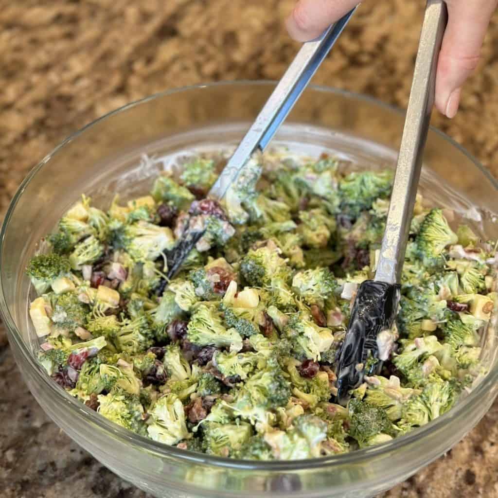 Mixing together broccoli salad in a bowl.