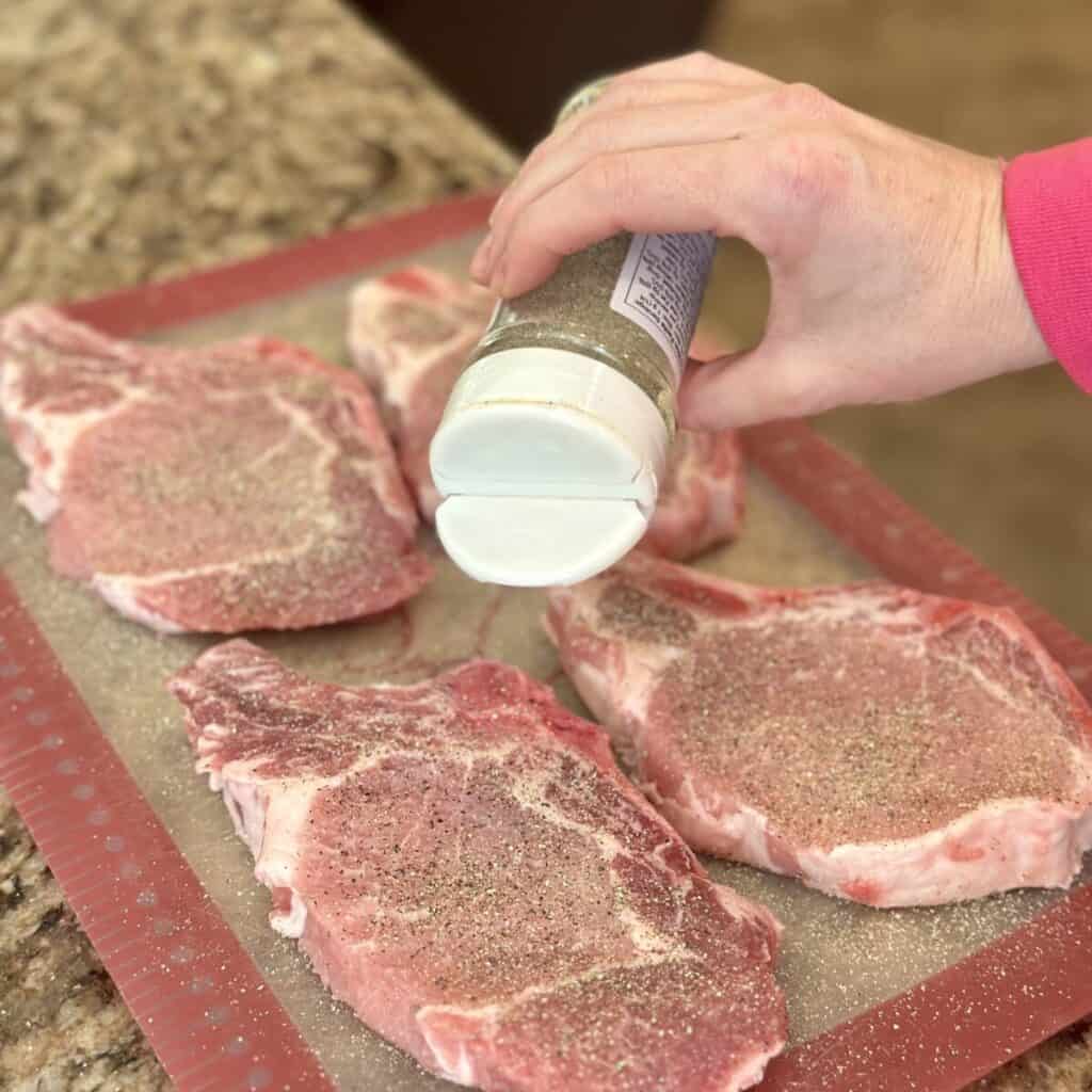 Seasoning pork chops on a cutting board.