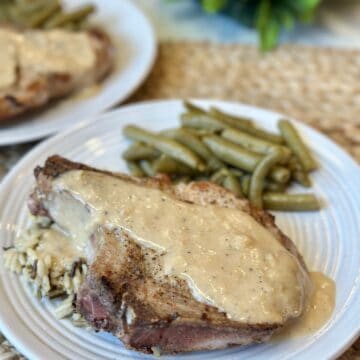 A pork chop on a plate with gravy, rice and green beans.