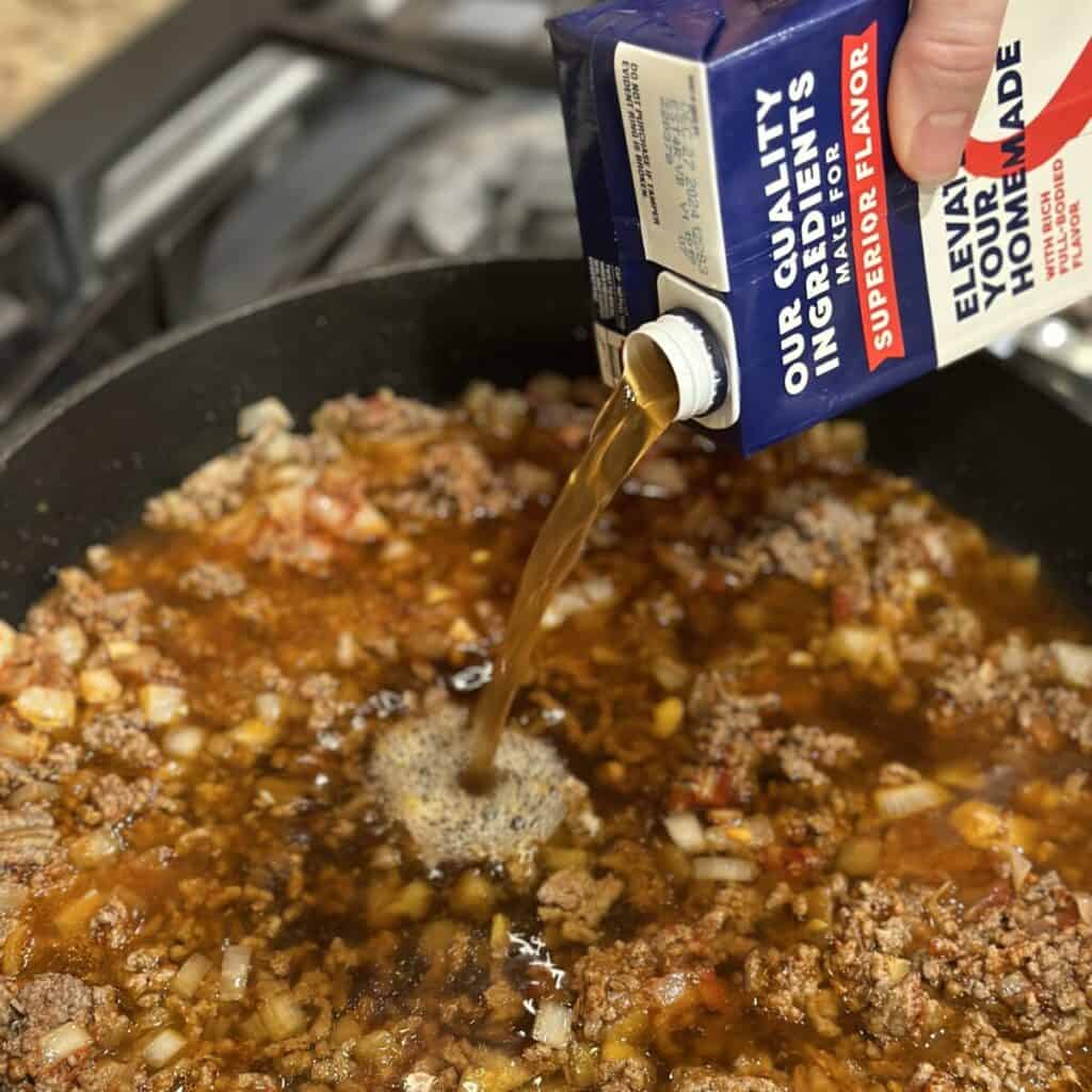 Adding beef broth to a skillet.