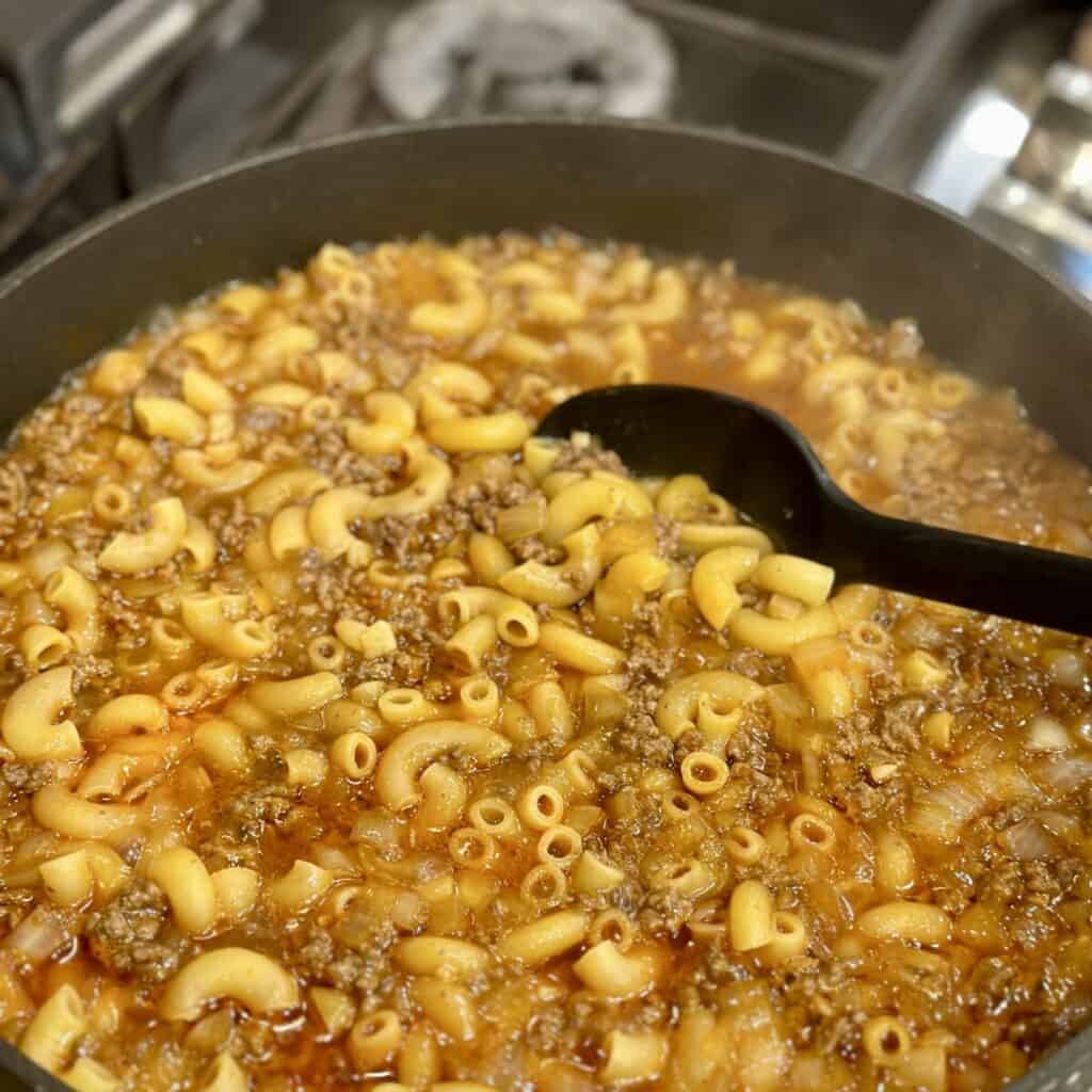Stirring noodles and beef in broth in a skillet.