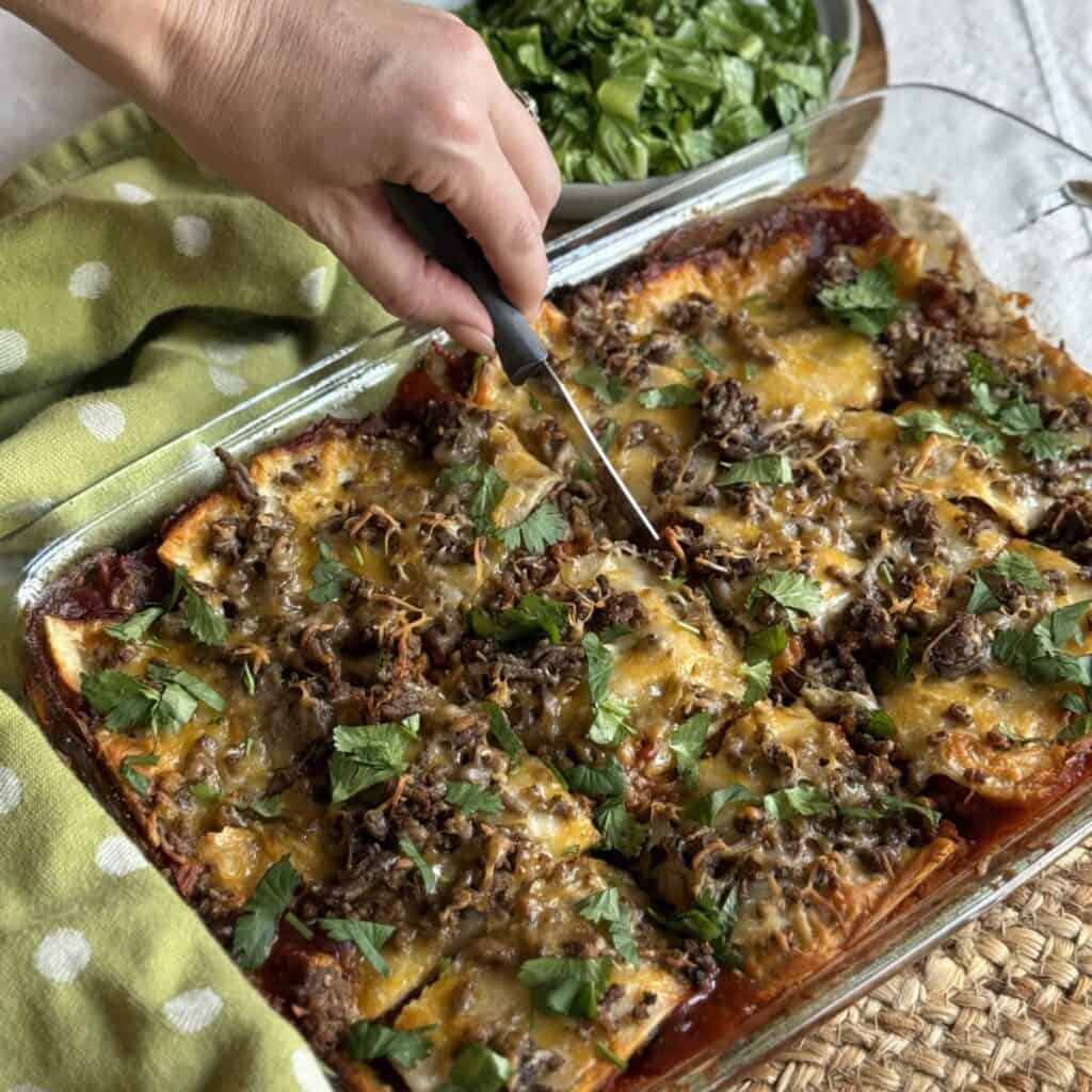 Slicing taco lasagna in a baking dish.