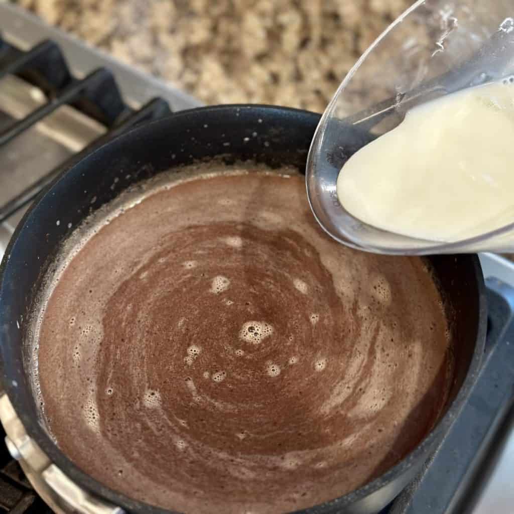 Adding milk to cocoa in a saucepan.