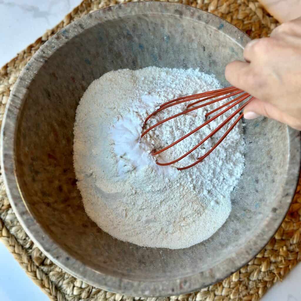 Mixing together flour and baking soda in a bowl.