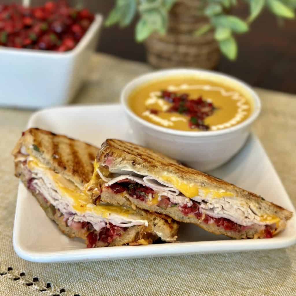 A close up shot of a turkey sandwich and soup with cranberry jalapeno salsa.