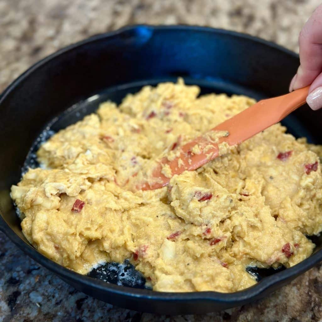 Spreading cornbread in a cast iron skillet.