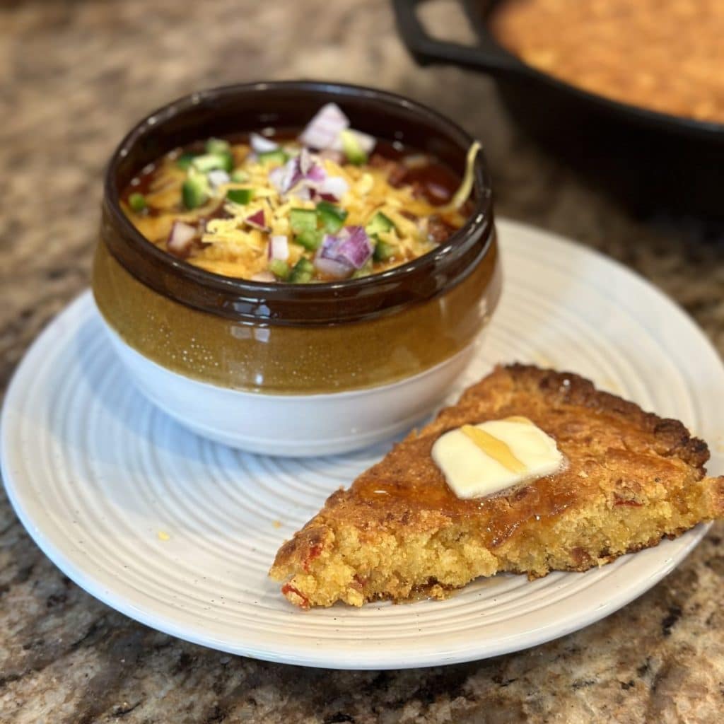 A slice of cornbread next to a bowl of chili.