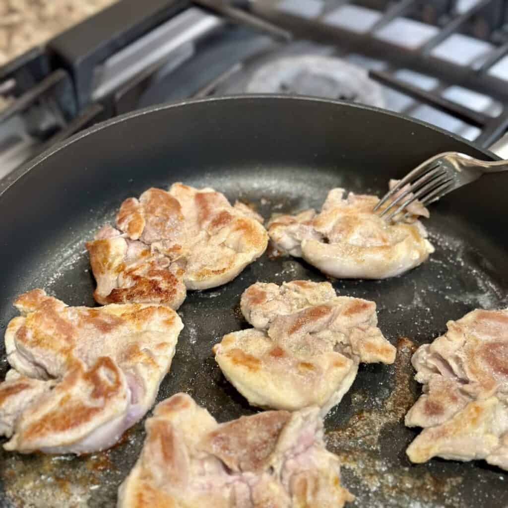 Searing chicken thighs in a skillet.