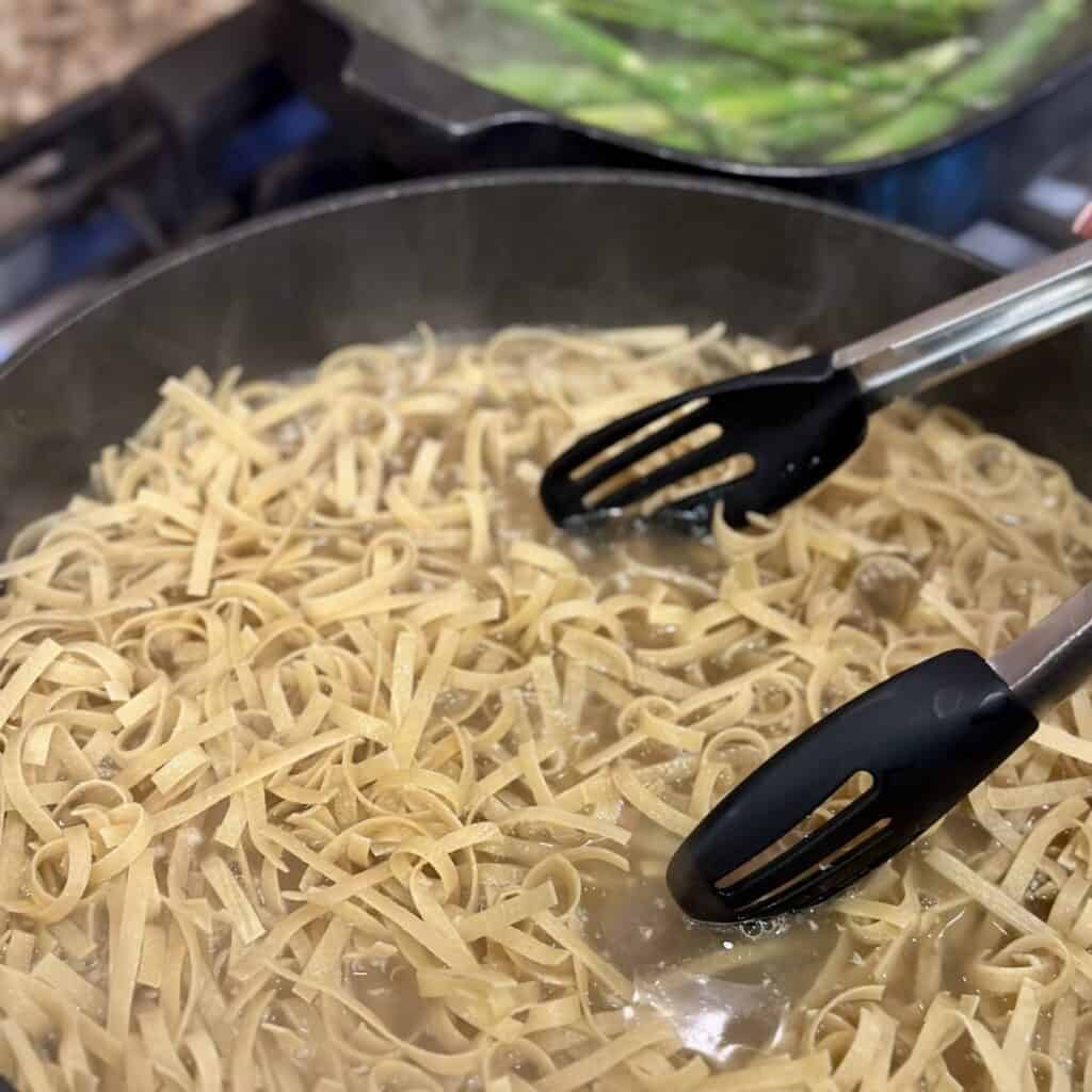 Cooking noodles in broth in a skillet.