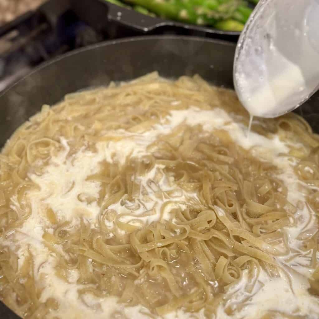 Adding cream to pasta cooking in a skillet.