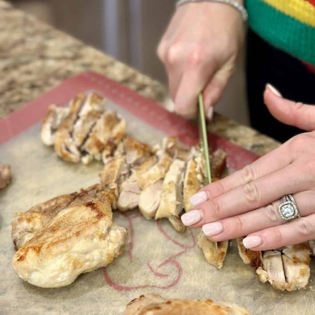 Slicing cooked chicken on a cutting board.