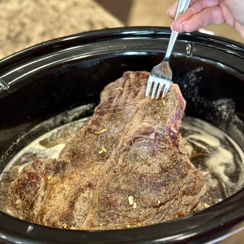 Adding a seared roast beef to a crockpot of broth.