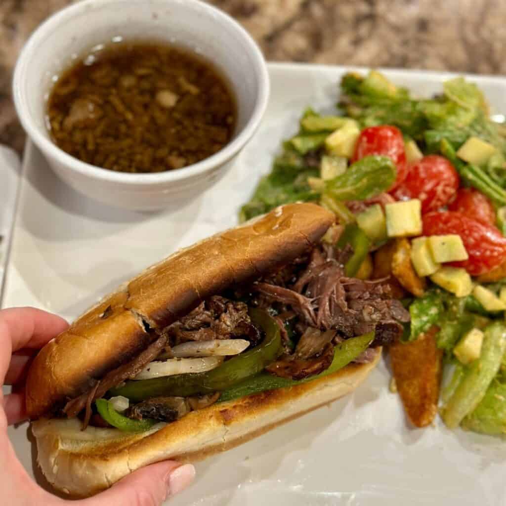 Grabbing a French dip sandwich on a plate.