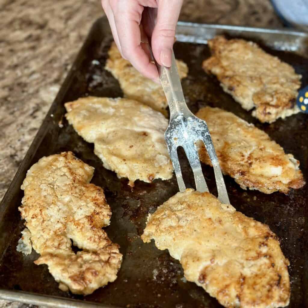 Flipping oven fried chicken on a sheet pan.