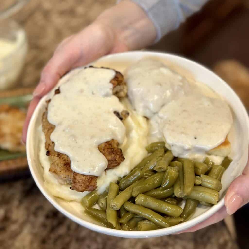 Holding a dinner plate of fried chicken and gravy.