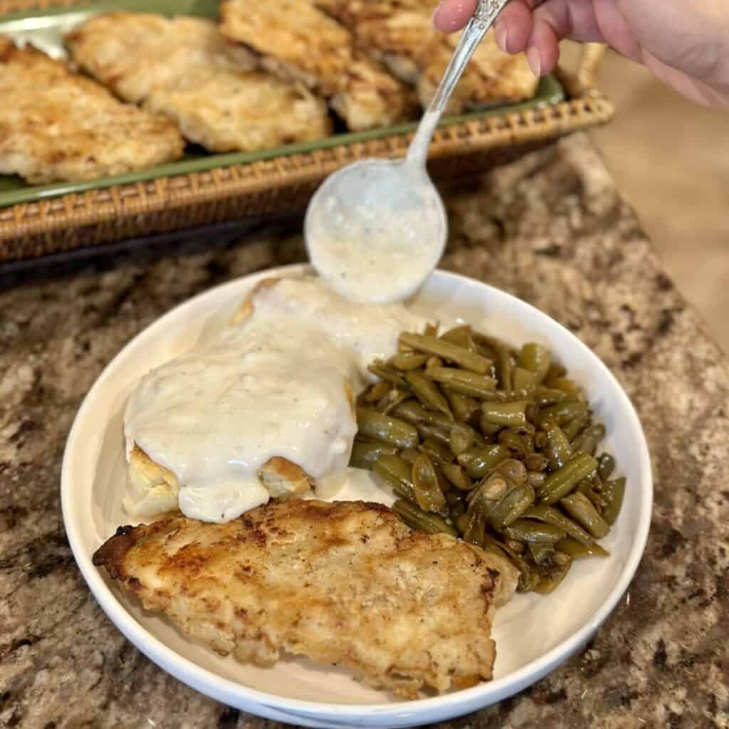 A plate of oven fried chicken, biscuits and gravy and green beans.