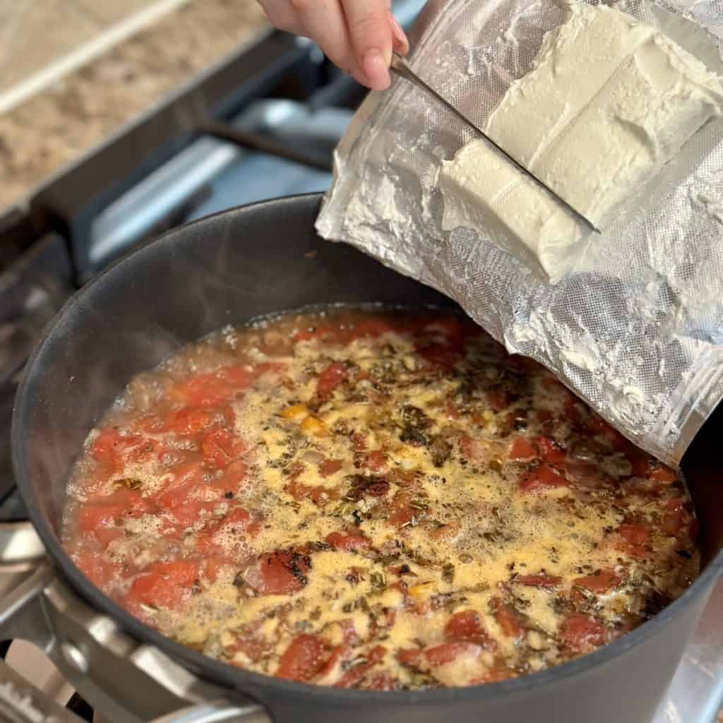 Adding cream cheese to a pot of soup.