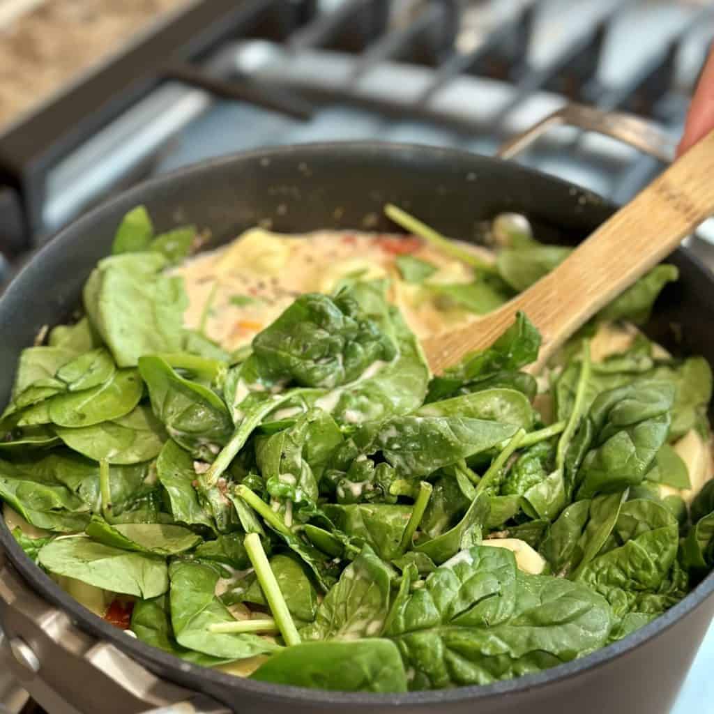 Adding spinach to a pot of soup.