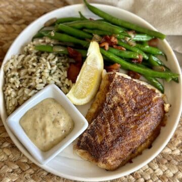 Blackened cod on a plate with beans and rice.