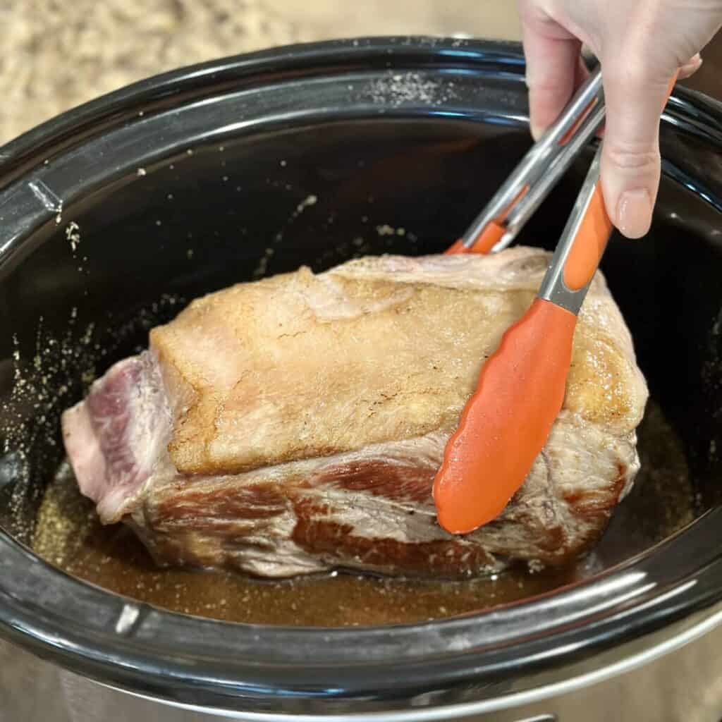 Adding a pork shoulder to a crockpot.