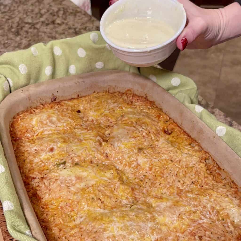 preparing to drizzle queso over a cooked pan of chicken and rice