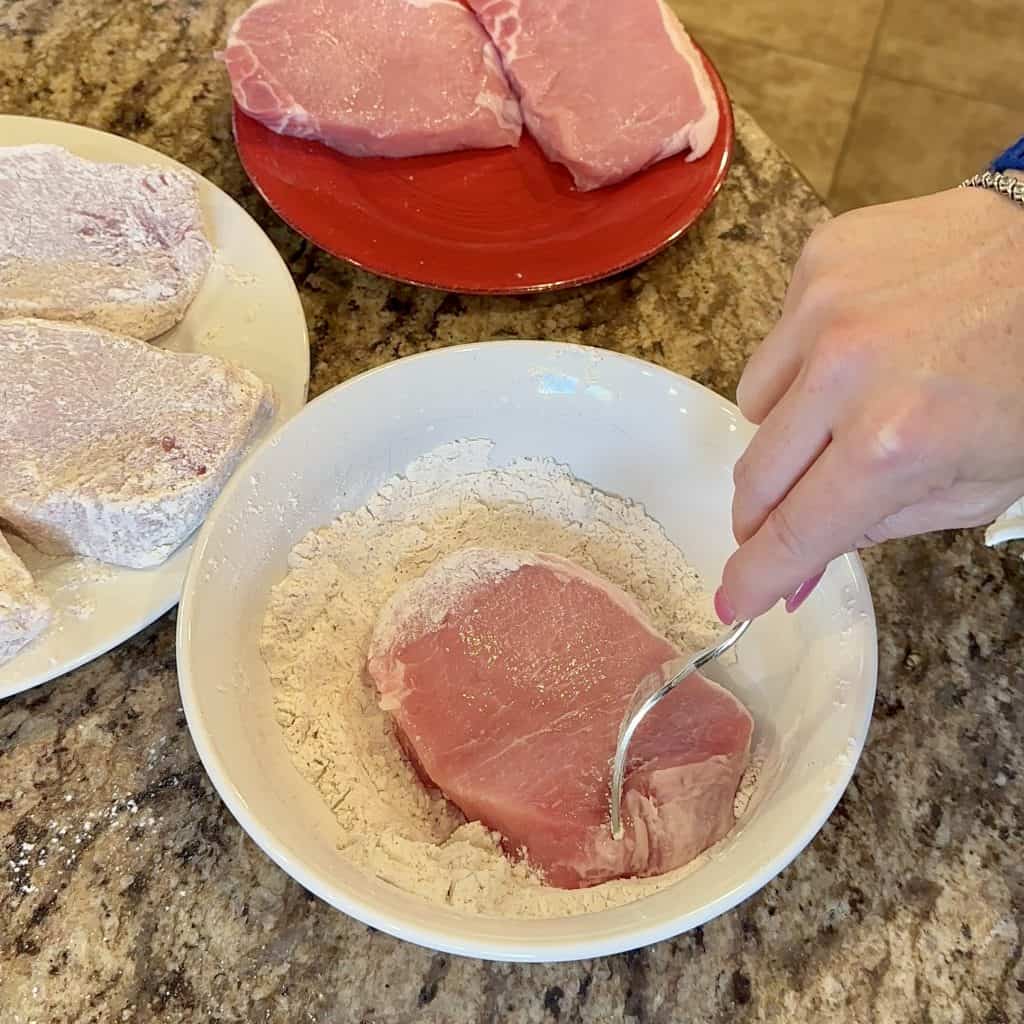 raw porkchops being dredged in flour and seasoning