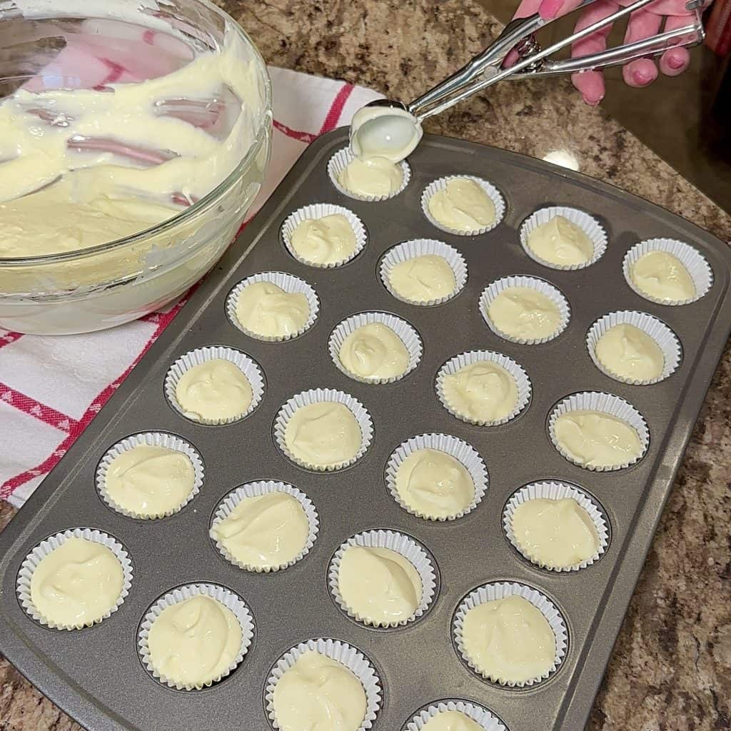 using a scoop to fill cupcake liners with one bite cheesecake filling