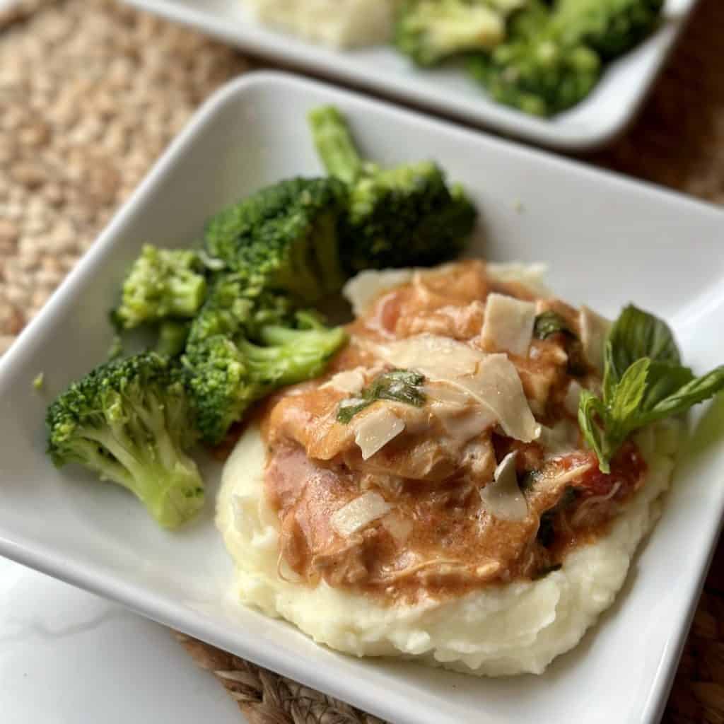 A plate of mashed potatoes topped with tomato chicken and served with broccoli.