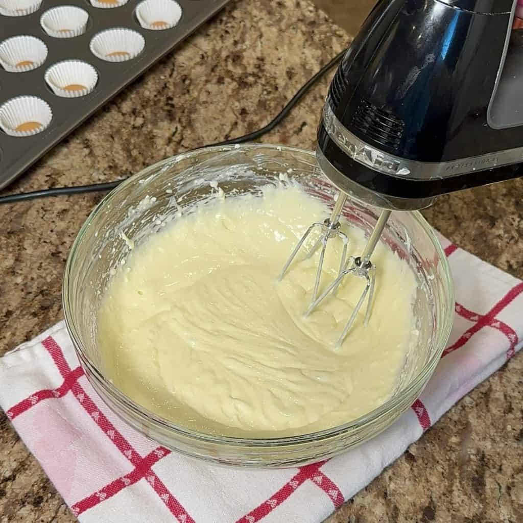 Mixing together cream cheese, eggs and sugar in a bowl with a mixer.