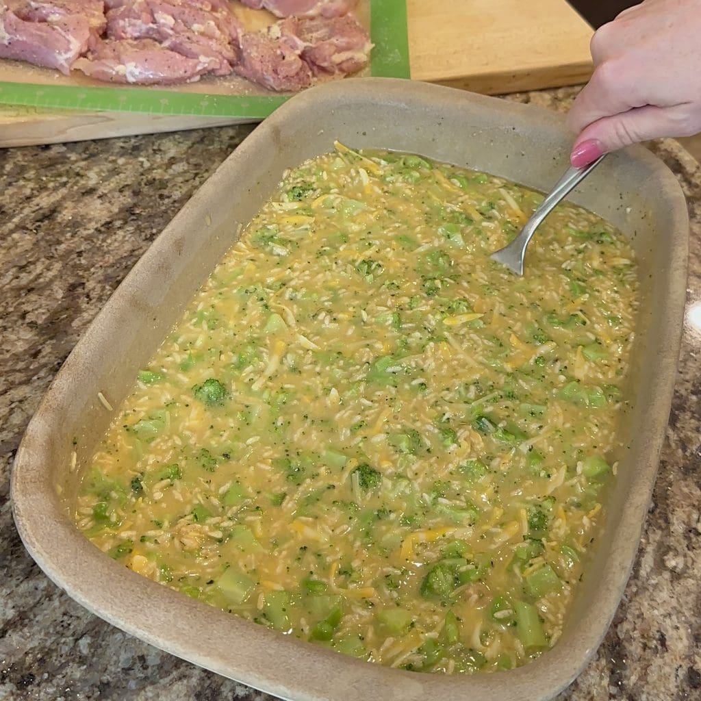 mixing the ingredients for cheddar  broccoli chicken and rice in a baking dish