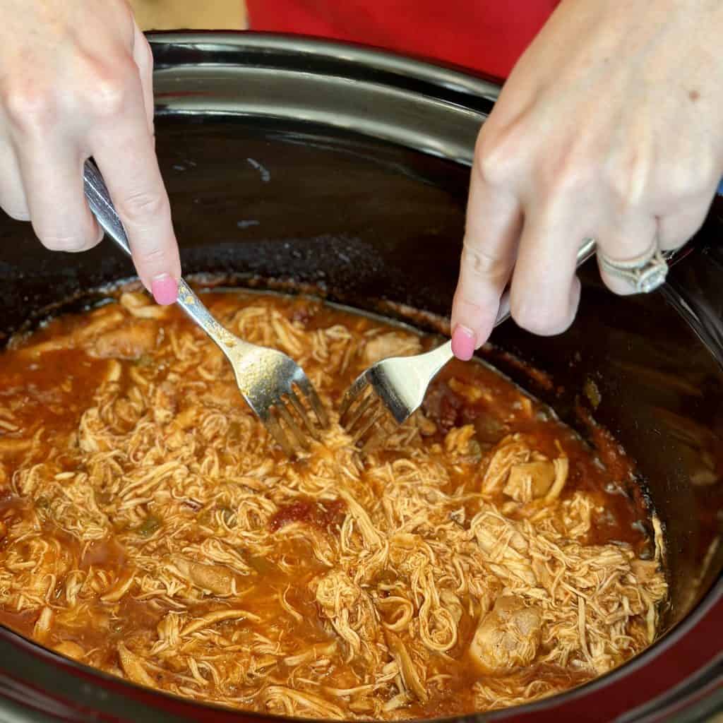 shredding the chicken with a pair of forks