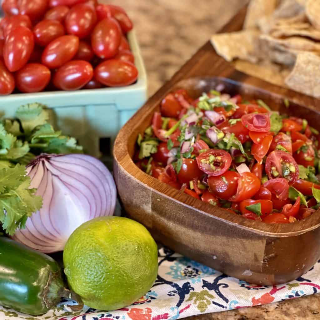 fresh pico de gallo with chips is displayed with the ingredients to prepare