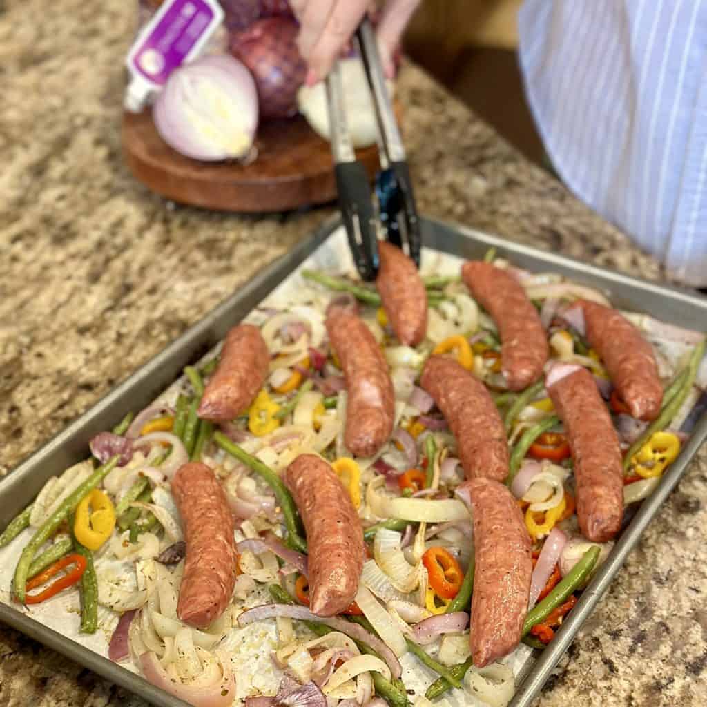 arranging sausages on top of the par-cooked veggies