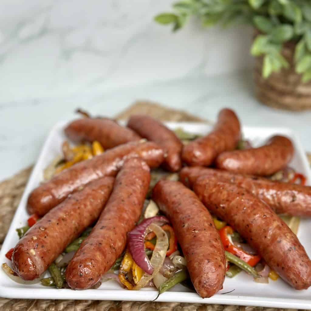 several whole links of sausage arranged over roasted onions and vegetables