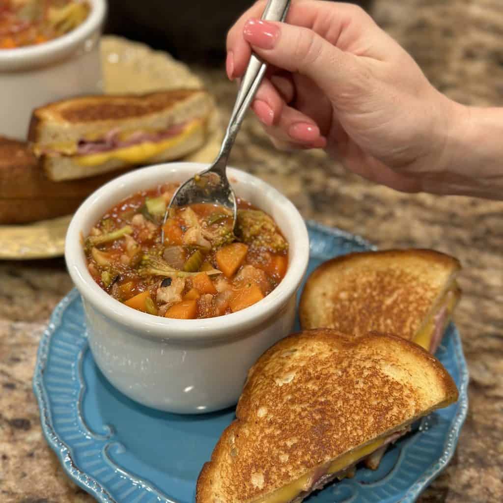 Loaded vegetable soup served in a bowl with a grilled cheese sandwich on the side