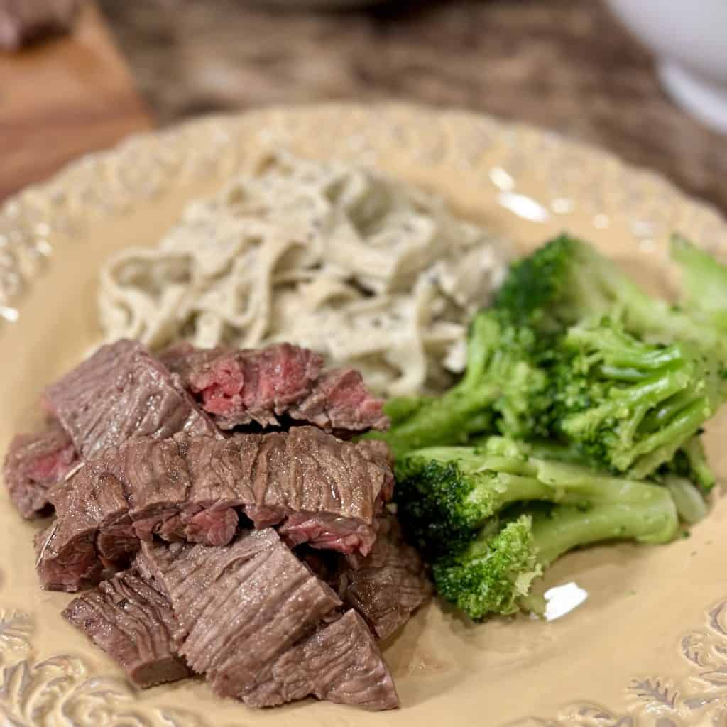 Plated marinated, sliced flank steak, served with noodles and steamed broccoli